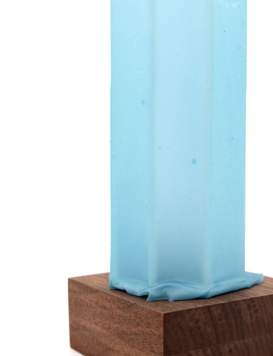 A close view of the aqua column on its walnut base, the faceted sides and the pooled, rippling foot filling the frame.