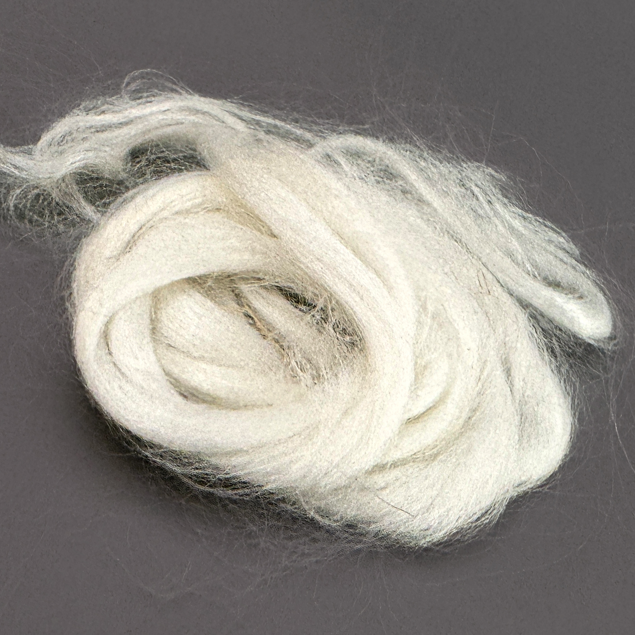 A length of soft white bamboo viscose roving coiled loosely into a nest, the fibre silky and faintly lustrous, with fine wisps drifting out from the mass.