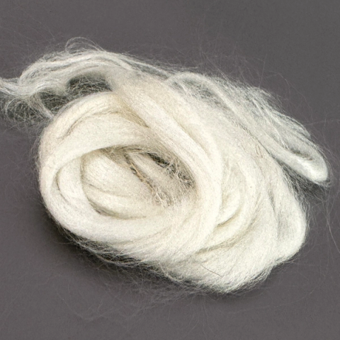 A length of soft white bamboo viscose roving coiled loosely into a nest, the fibre silky and faintly lustrous, with fine wisps drifting out from the mass.