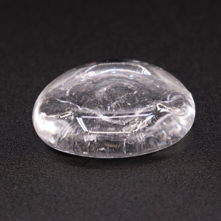 A single clear lump of glass on a dark ground, its domed surface smooth with swirling internal ripples and a folded seam along one side.