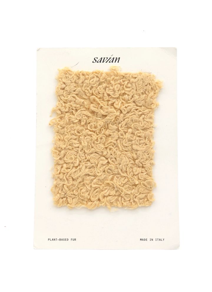 A swatch of dense looped plant-based fur in pale cream, mounted on a card printed “savian — plant-based fur, made in Italy”.