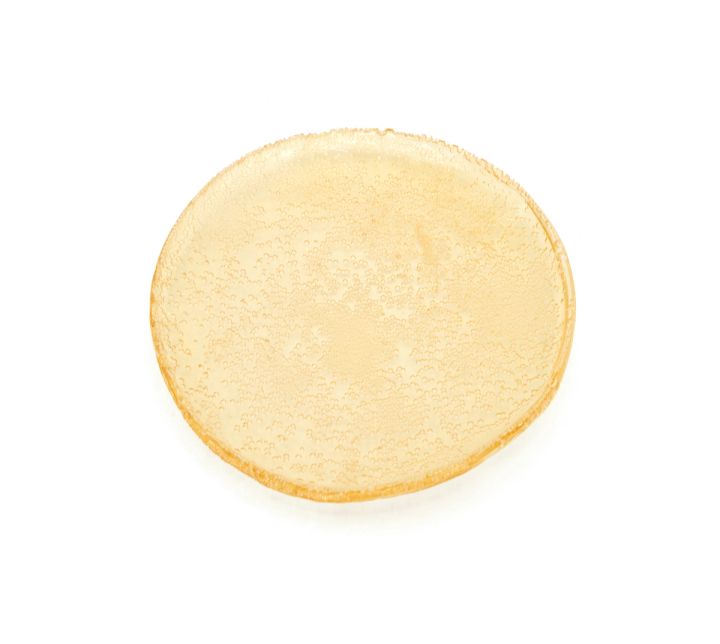 A single disc of pale amber bioglass seen face-on, its rim rippled and its surface finely crazed.