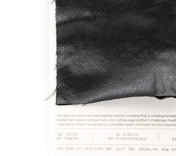 The black swatch seen closer against its card, the pebbled grain and stitched edge clear, the card reading “no toxins, no tanning, no plastic, no petrochemicals”.