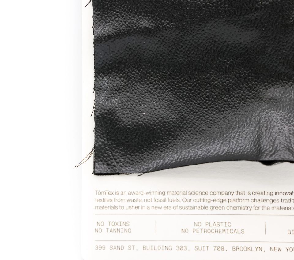 The black swatch seen closer against its card, the pebbled grain and stitched edge clear, the card reading “no toxins, no tanning, no plastic, no petrochemicals”.