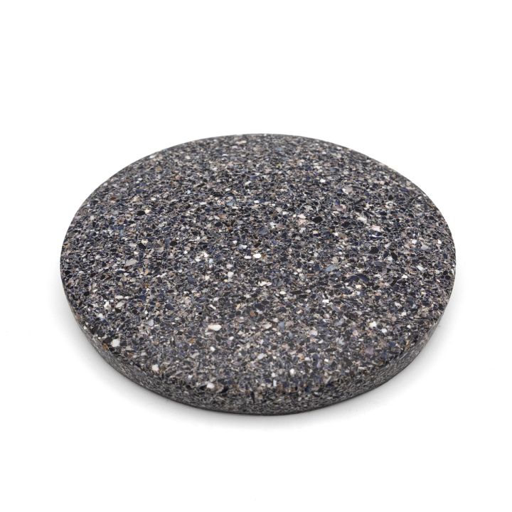 The tile at an angle, its charcoal speckled face and the full depth of its edge both visible.
