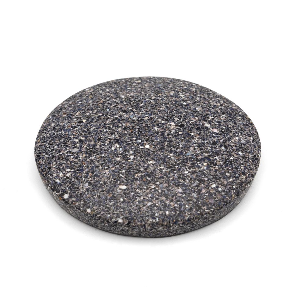 The tile at an angle, its charcoal speckled face and the full depth of its edge both visible.