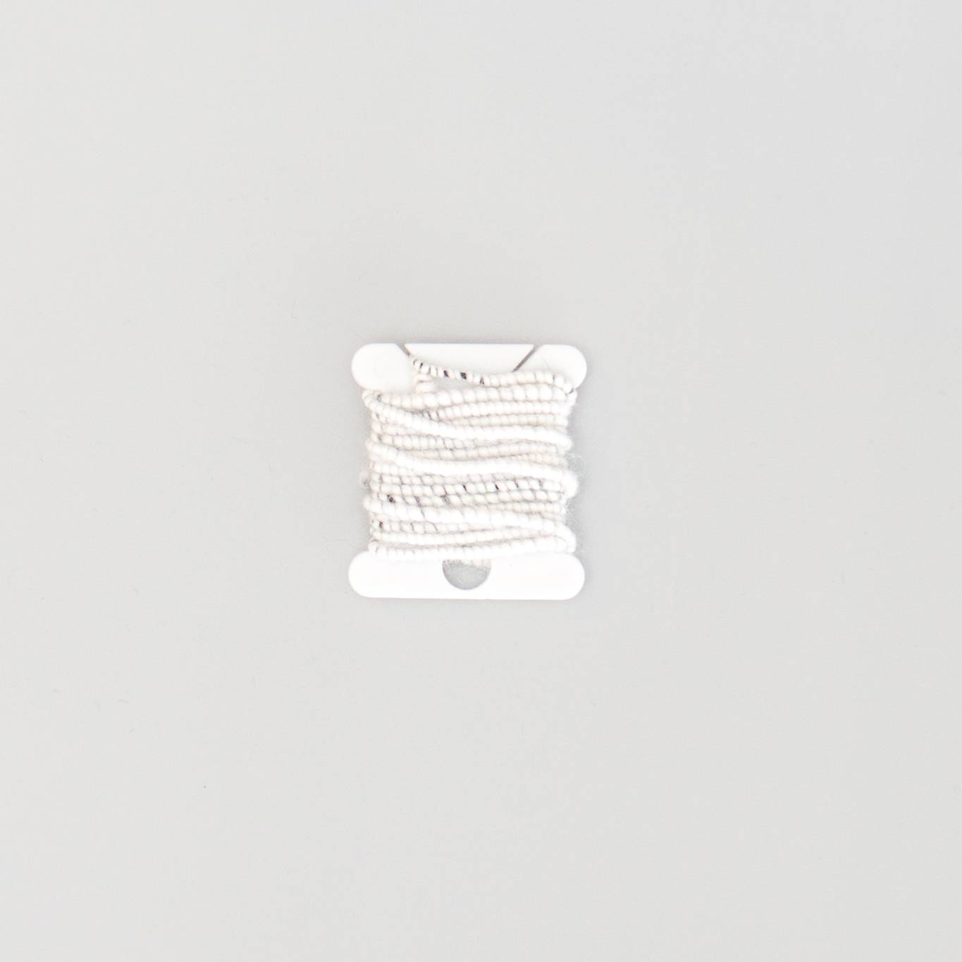 A short length of white beaded cord wound onto a small white bobbin, the coiling giving it a knobbly, segmented look.
