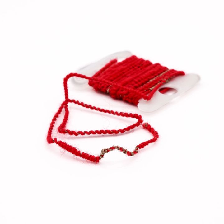 The bobbin from another angle with the loop of yarn spread wider, so the bare silver wire twisting along one section reads clearly.