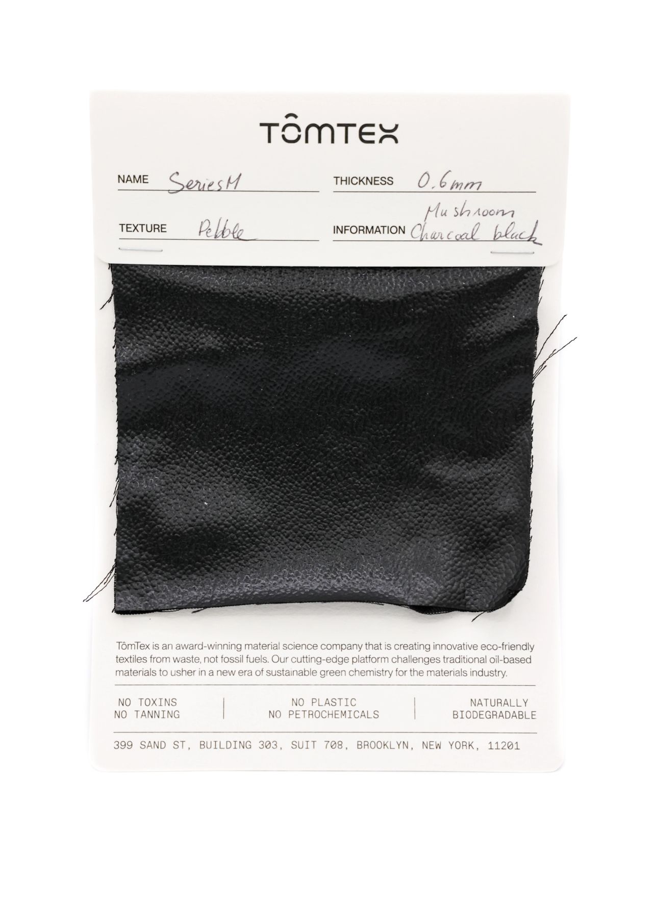 A black leather-like swatch with a fine pebbled grain, stapled to a TômTex specification card recording Series M, 0.6 mm thickness, a pebble texture and mushroom charcoal black.