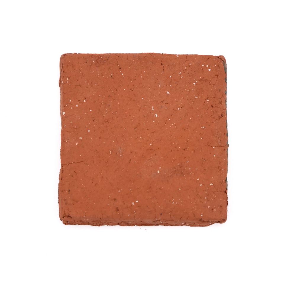 A square fired slab in bright brick orange, its surface slightly rough with small white flecks and a hairline crack near the top.
