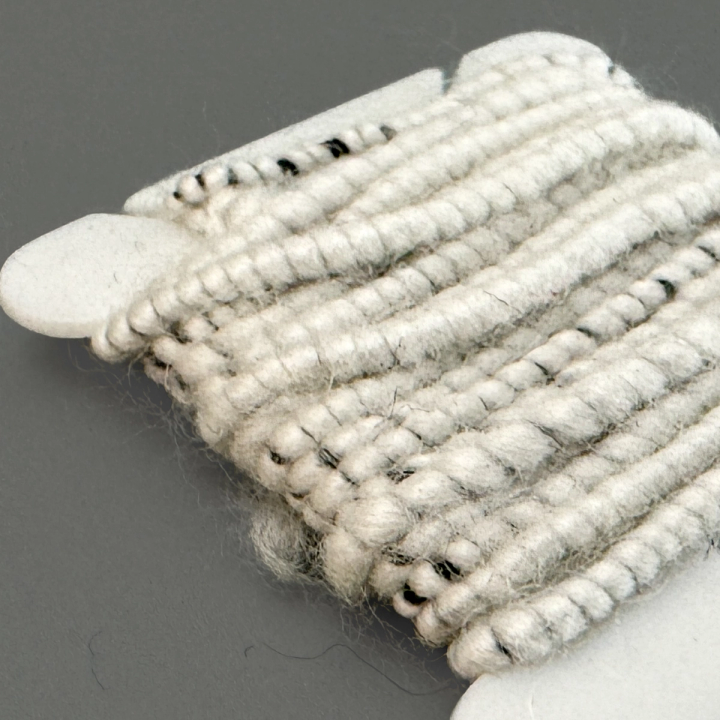 The wound cord against a dark ground, the coils thick and woolly with grey and black fibre showing through.