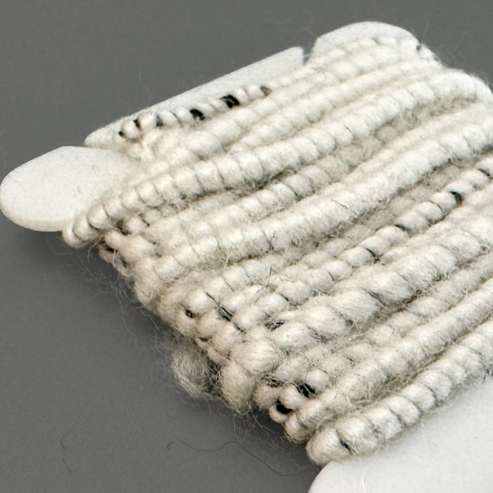 The wound cord against a dark ground, the coils thick and woolly with grey and black fibre showing through.