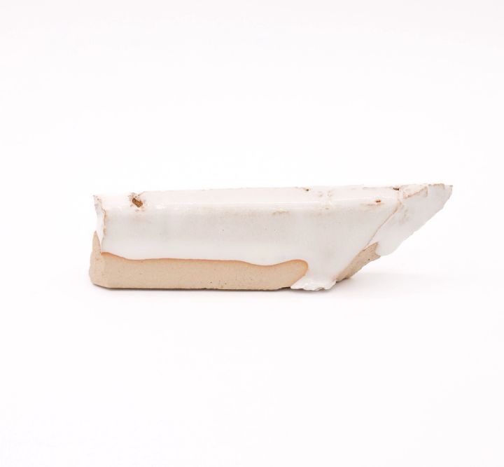 A shard seen edge-on, a thick glossy white glaze pooling over pale buff clay and running past the broken edge.
