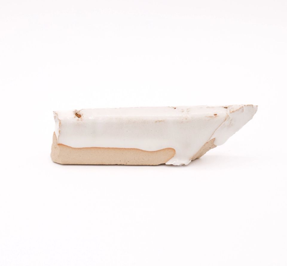 A shard seen edge-on, a thick glossy white glaze pooling over pale buff clay and running past the broken edge.