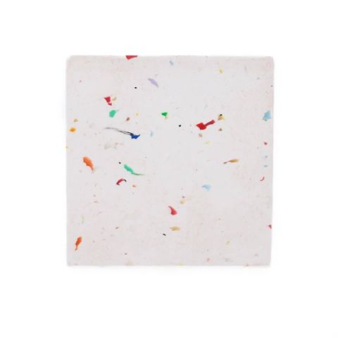 A square tile of white recycled plastic, its surface scattered with small bright flecks of red, blue, green and yellow.