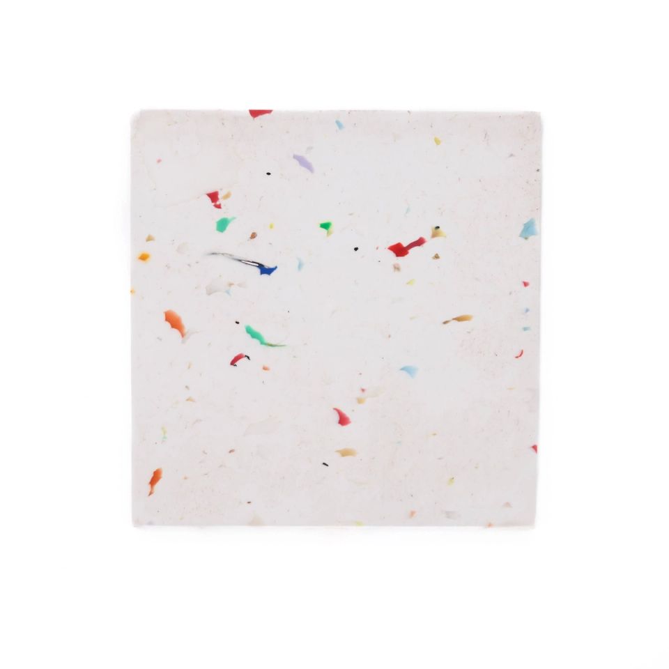 A square tile of white recycled plastic, its surface scattered with small bright flecks of red, blue, green and yellow.