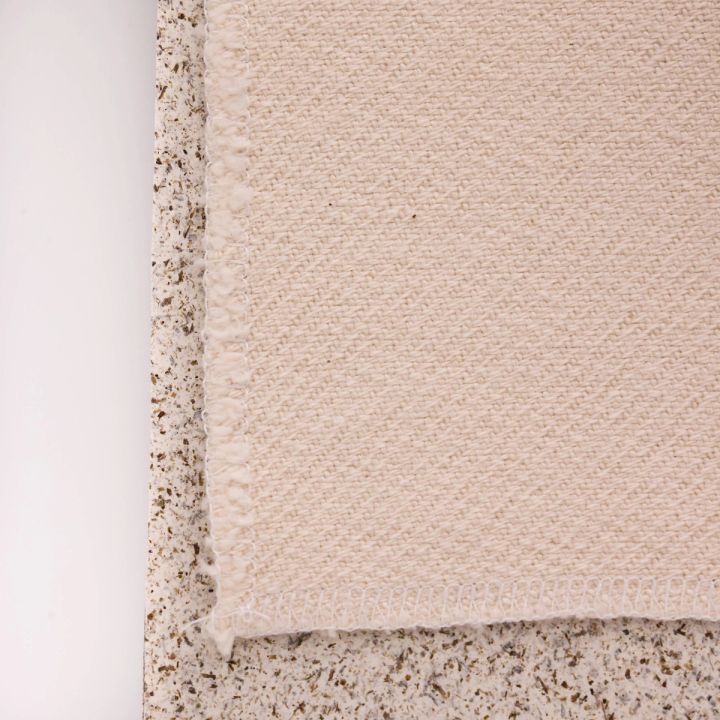 A close view of one corner, the basket weave's diagonal texture and finished hem clear against the speckled board.