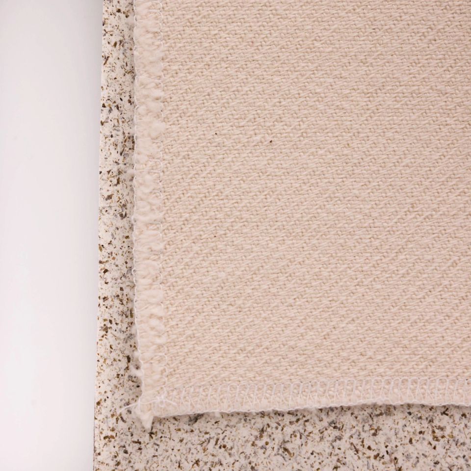 A close view of one corner, the basket weave's diagonal texture and finished hem clear against the speckled board.