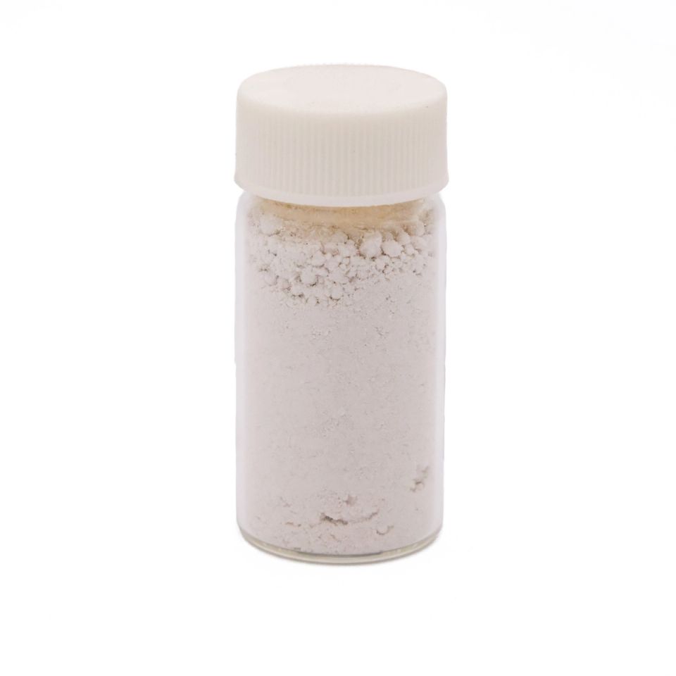 A clear glass vial with a ribbed white screw cap, filled with fine off-white powder that clumps softly near the top and carries a faint sandy tint.