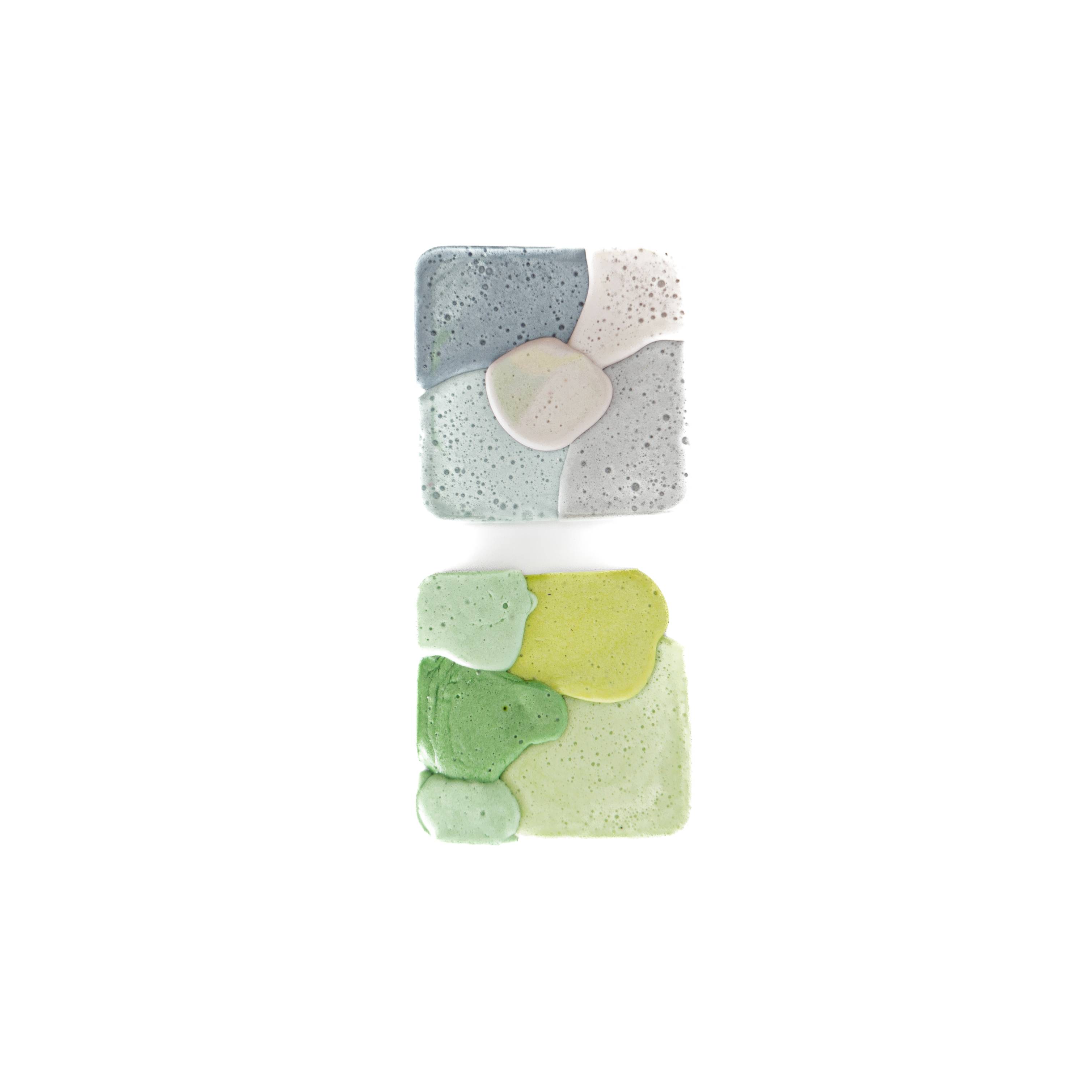 Two small square samples: the upper one grey-blue with a smooth pale inset, the lower one mottled in greens, both surfaces finely pitted.