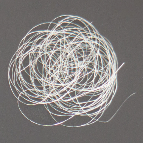 A loose tangle of fine translucent filaments coiled into a flat nest, catching the light in faint rainbow glints along their lengths.