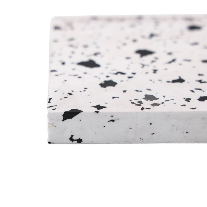A thick tile of white recycled plastic at an angle, its surface scattered with irregular black flecks and its cut edge plain white.