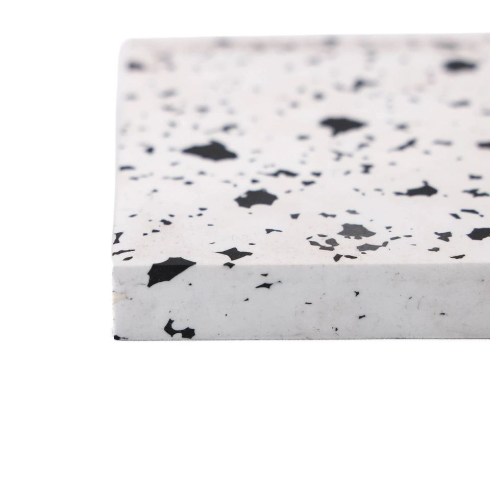 A thick tile of white recycled plastic at an angle, its surface scattered with irregular black flecks and its cut edge plain white.
