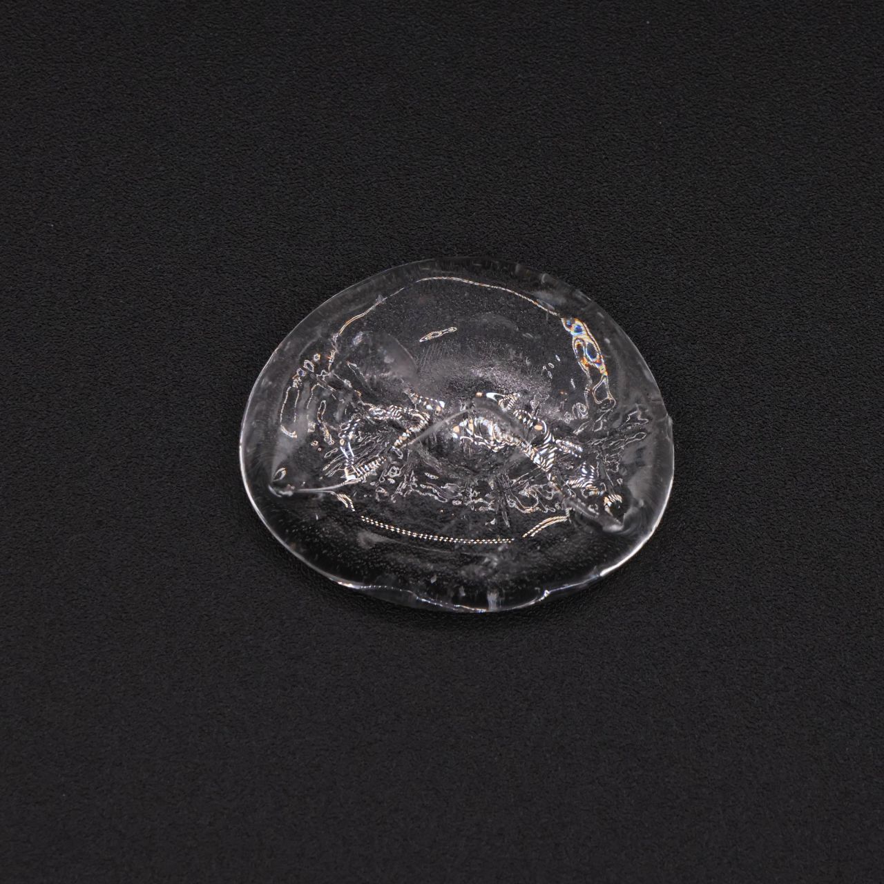A small clear disc of glass with a rippled, bubbled surface and a few flecks of colour caught inside.