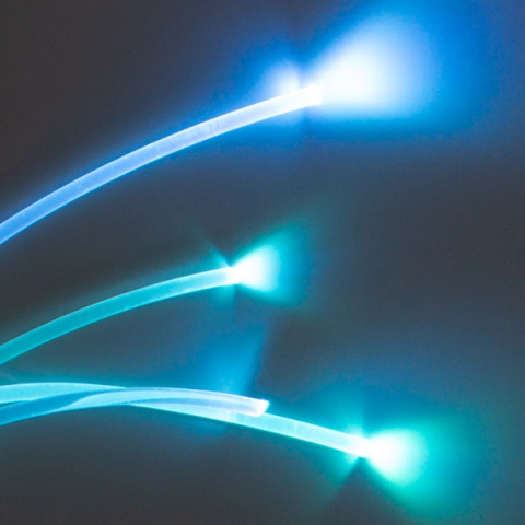Three fibre-optic strands curving through darkness, each glowing along its length in blue and turquoise and flaring to a bright white point at the tip.