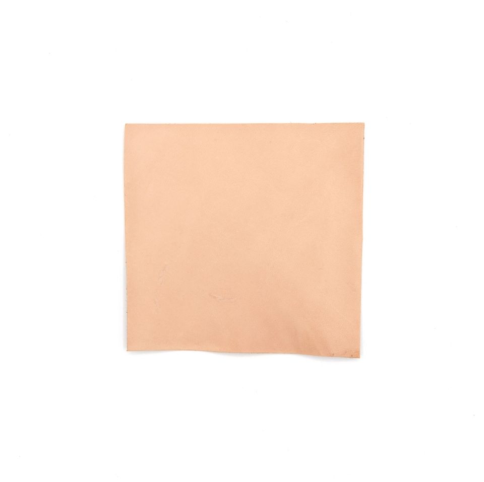 A square of chrome-tanned bison leather in soft blush pink, its surface smooth and matte, one corner curling slightly.