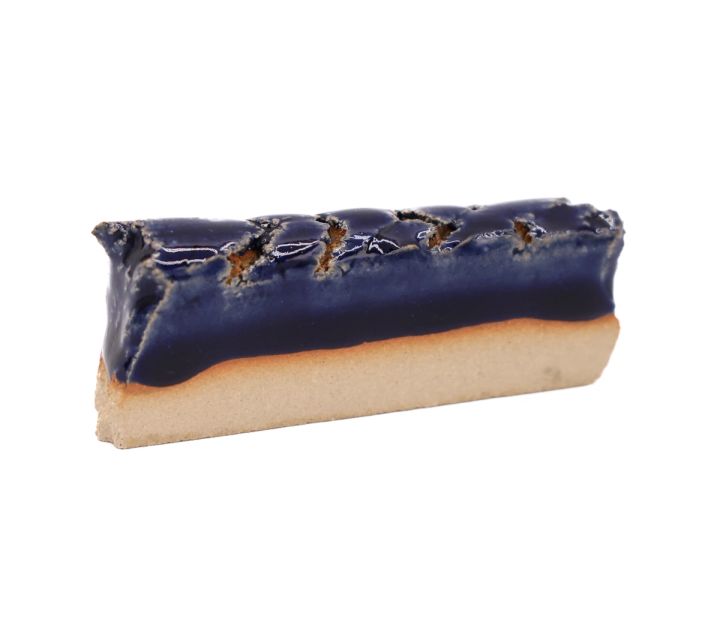 A shard seen edge-on, a deep cobalt glaze lying thickly over buff clay, its upper surface blistered and split.
