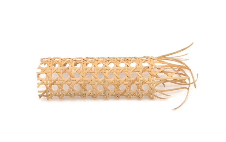 A length of machine-woven cane webbing rolled into a loose tube, its open hexagonal lattice pale honey-coloured, with cut strands fanning out at one end.