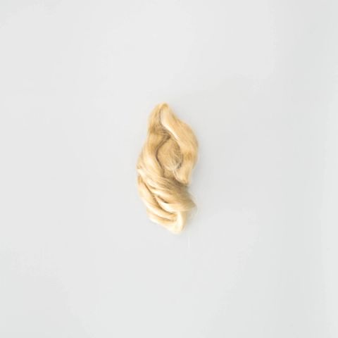 A small twist of tussah silk in warm honey-gold, its filaments smooth and lustrous, gathered into a soft flame-like curl.