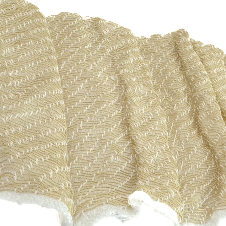 A close view of the same linen, its crimped weave filling the frame in cream and pale gold and drawn into deep vertical folds.