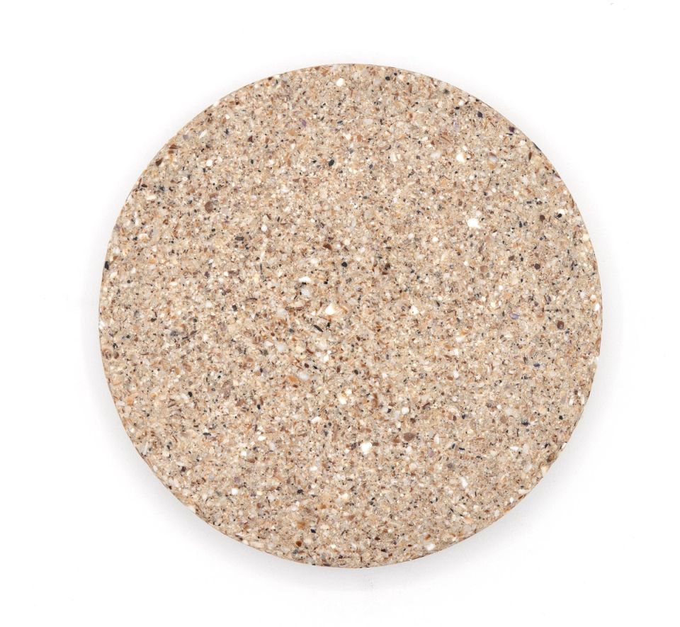 A larger round tile of dense composite in pale oatmeal, evenly speckled with fine crushed shell.