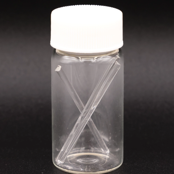 The vial against a dark ground, the two fine glass rods crossing inside it and catching a bright highlight.