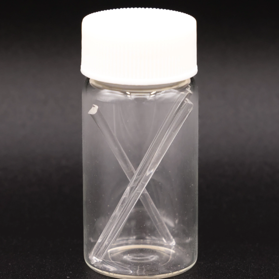 The vial against a dark ground, the two fine glass rods crossing inside it and catching a bright highlight.