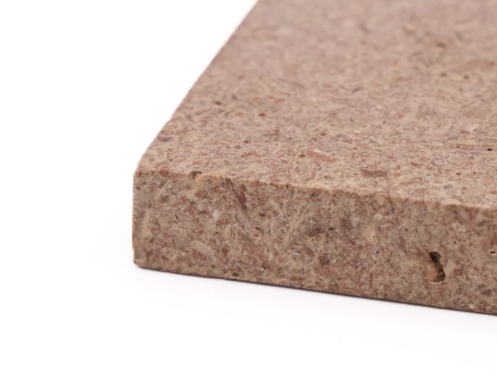 A close view of the tile's corner, the speckled brown surface meeting a thick cut edge dense with pale fibrous flecks.