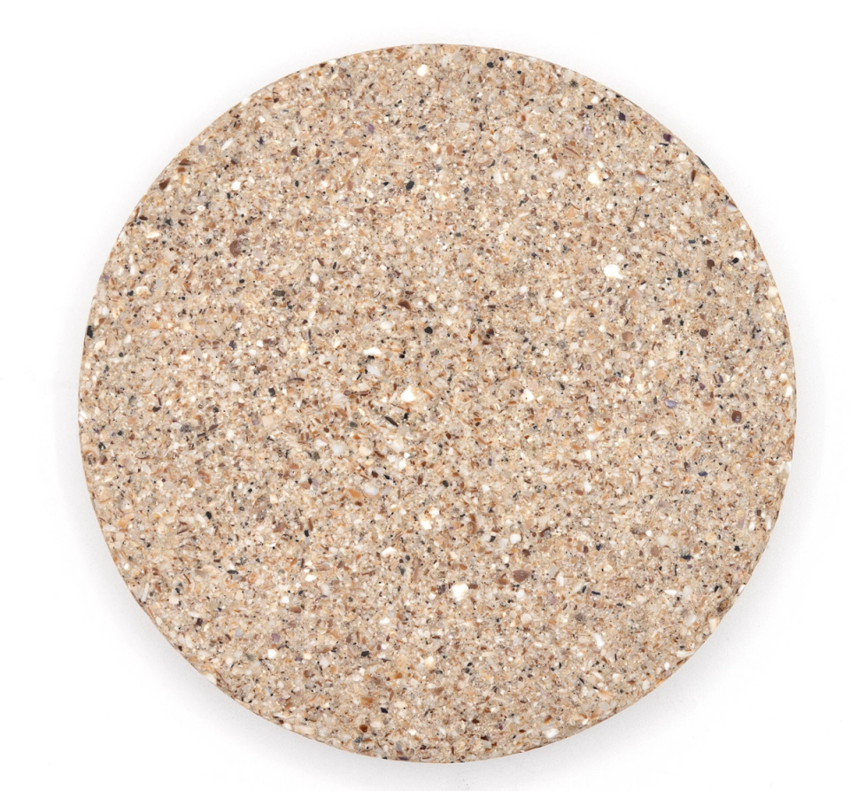 A round tile of dense composite in warm sandy beige, thickly studded with crushed shell in cream, white and grey.