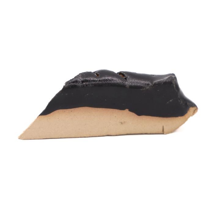A smaller broken shard seen edge-on, a glossy black glaze lying thickly over pale buff clay.