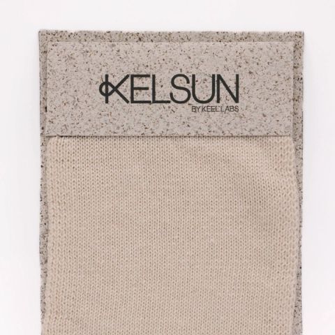 A knitted swatch in undyed cream, stocking stitch running vertically, mounted on a speckled grey board printed “KELSUN by Keel Labs”.