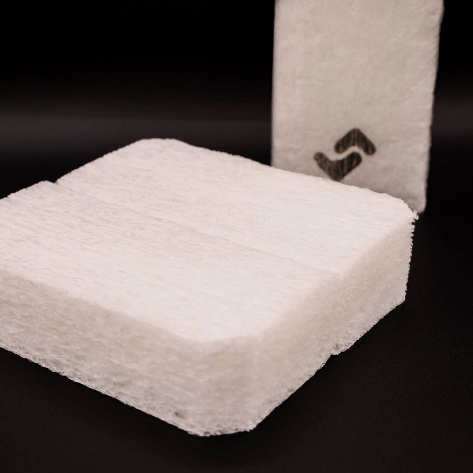A thick slab of white biofoam with a coarse, fibrous cut face, a second piece standing upright behind it marked with a dark zigzag.
