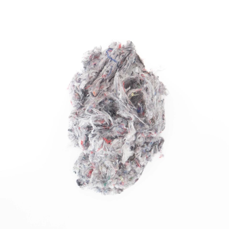 A loose clump of recycled fibre fill in pale grey, wiry and matted, shot through with flecks of red, blue and black.