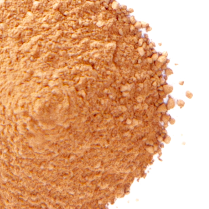A close view of the powder mounded high, its grains a warm rust orange, coarse and lumpy where they spill away at the edge.