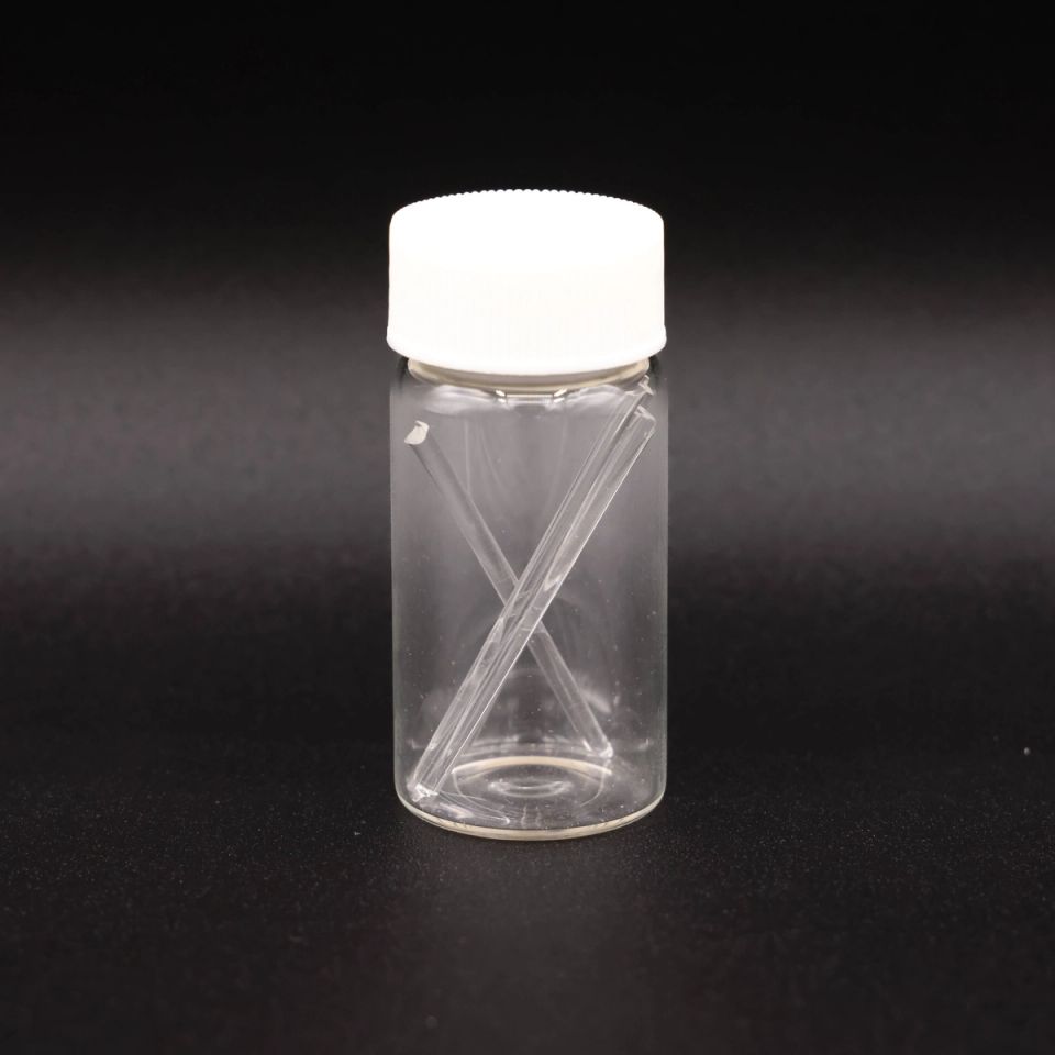 A clear glass vial with a white screw cap holding two fine glass rods crossed inside it.