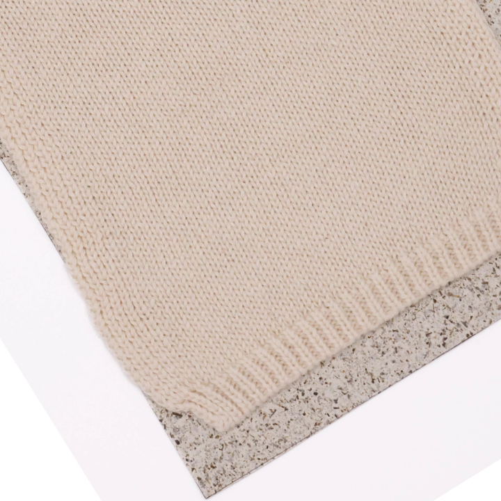 A close view of one corner, the fine knit stitches and the ribbed edge banding visible against the speckled board.