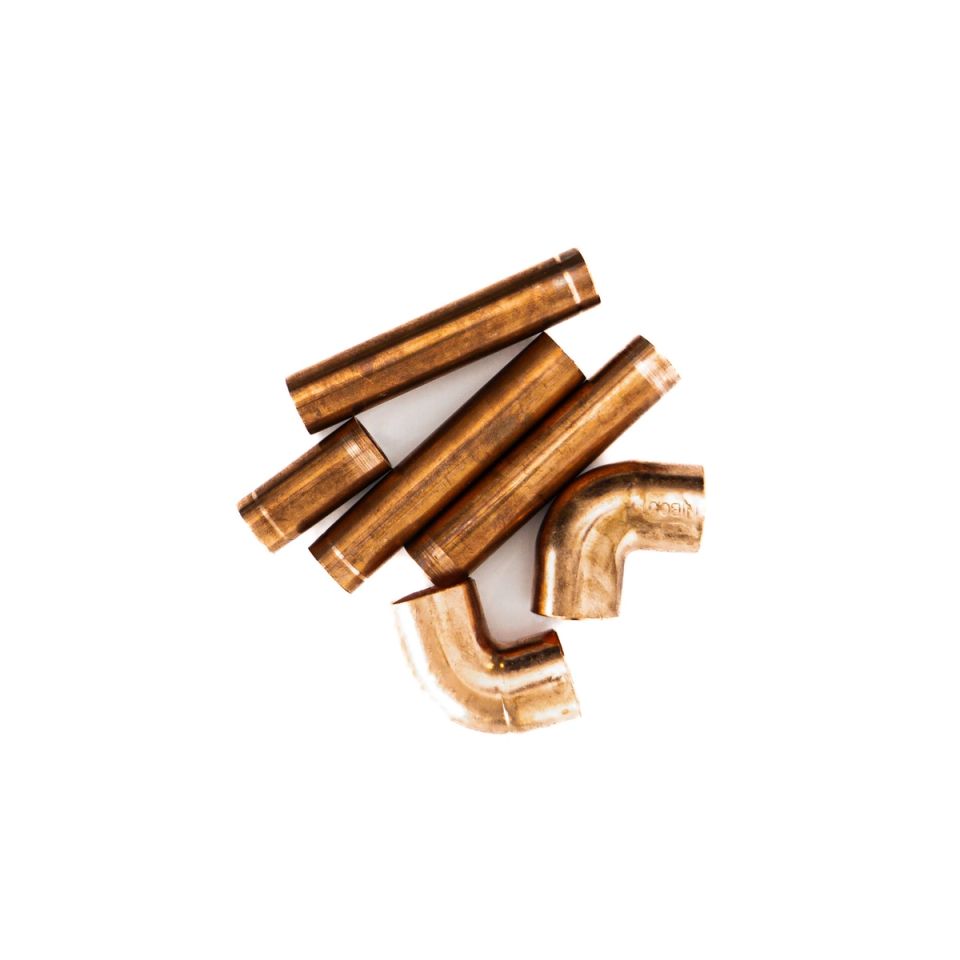 Six short lengths of copper pipe and two elbow fittings heaped together, their surfaces warm orange-gold and polished to a soft shine.