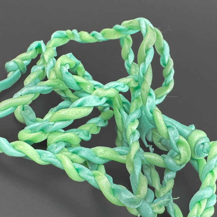 A close view of the extruded string, the mint-green strand twisted into a rope and looping over itself in a loose tangle.