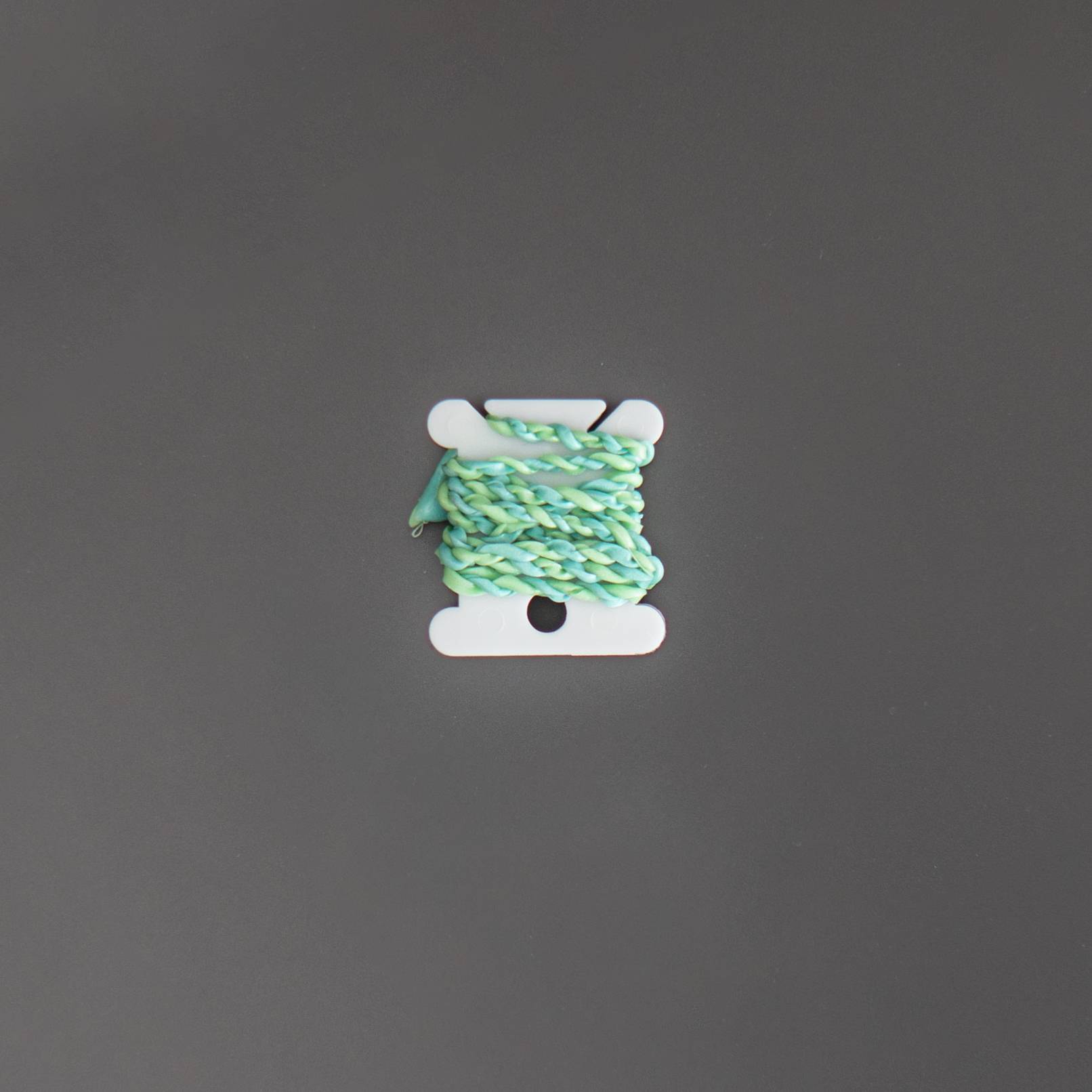 A short length of pale mint-green extruded string wound onto a small white bobbin, the strand twisted and slightly irregular.