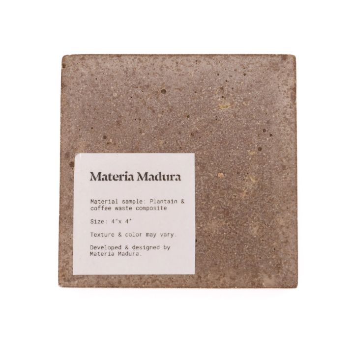 The tile face-on with a printed label reading “Materia Madura — Material sample: Plantain & coffee waste composite, Size 4″ x 4″. Texture & color may vary.”